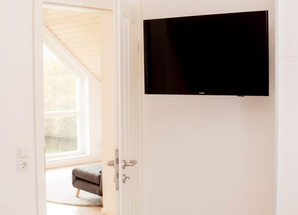 Schlafzimmer mit TV und Blick in den lichtdurchfluteten Wohnbereich